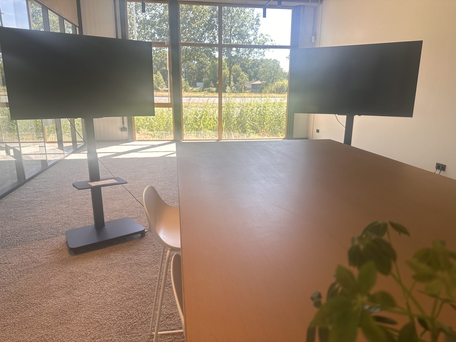 De vergaderruimte met grote tafel en twee schermen